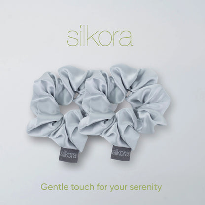 Twee grote Silkora scrunchies in zilvergrijs op een lichte achtergrond met het Silkora-logo en de tekst "Gentle touch for your serenity".