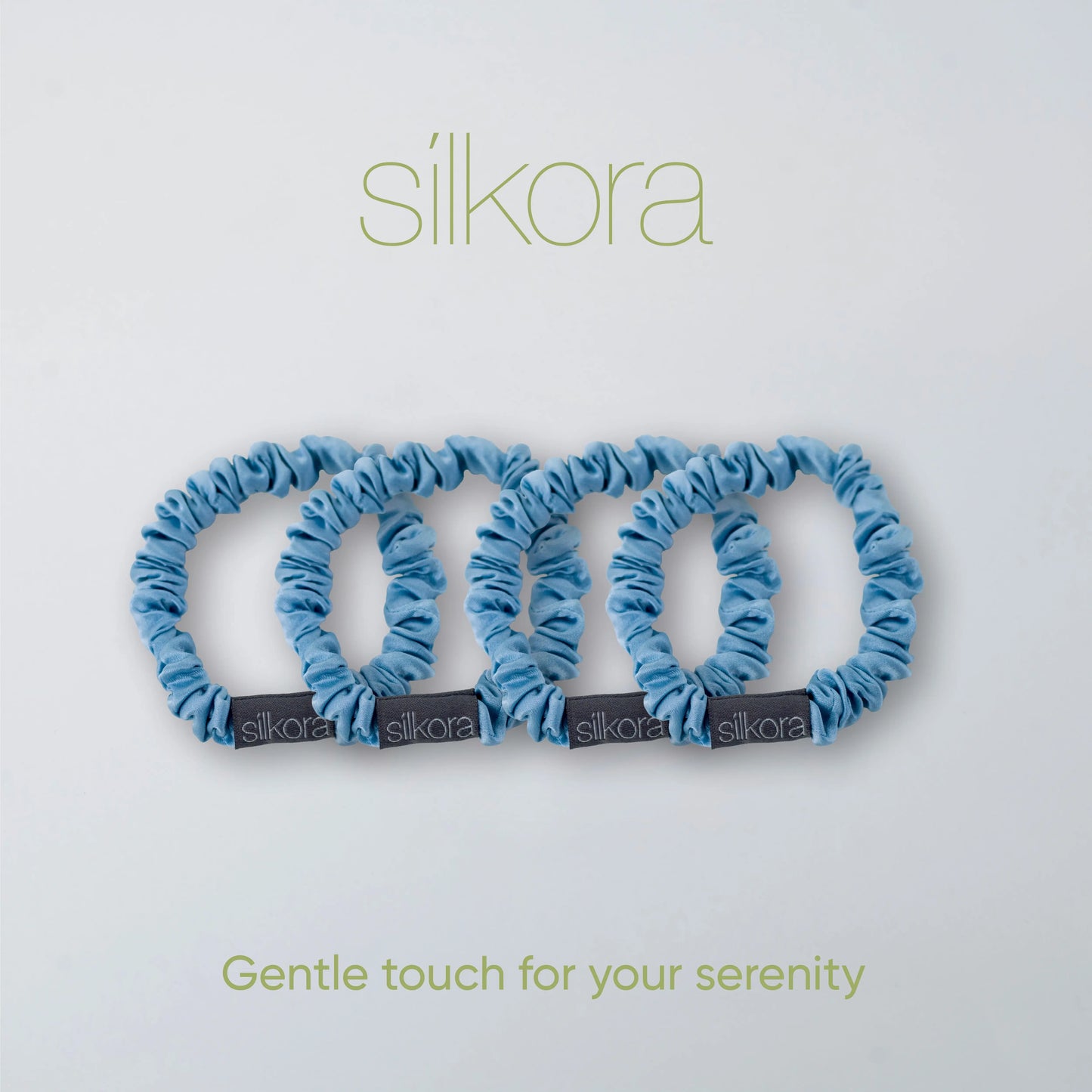 Vier kleine Silkora scrunchies in icy blauw op een lichte achtergrond met het Silkora-logo en de tekst "Gentle touch for your serenity".