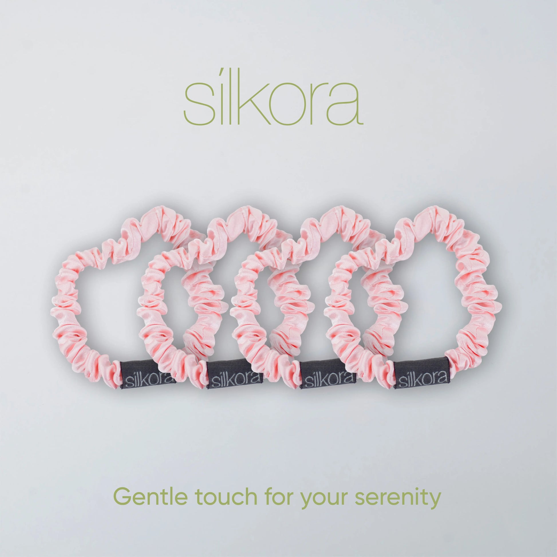 Vier kleine Silkora scrunchies in lotus roze op een lichte achtergrond met het Silkora-logo en de tekst "Gentle touch for your serenity".