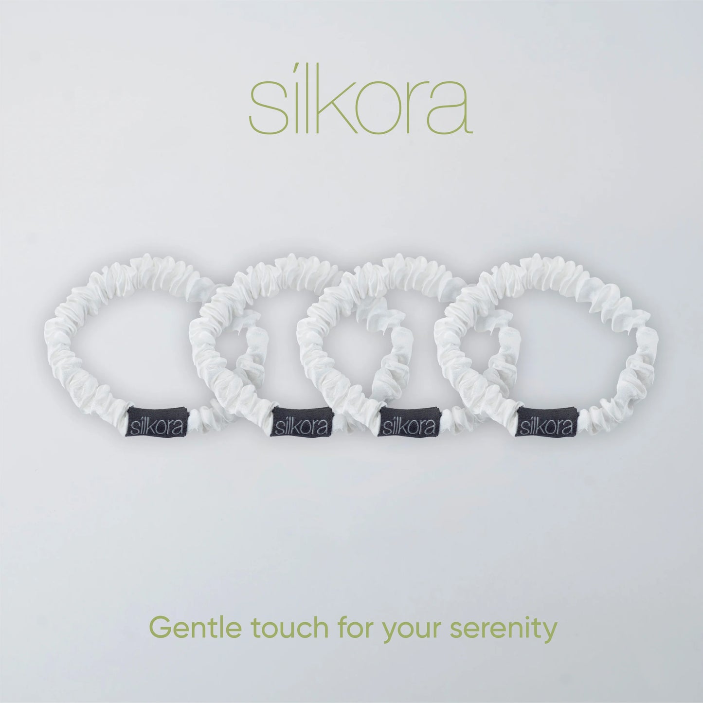 Vier kleine witte Silkora scrunchies op een lichte achtergrond met het Silkora-logo en de tekst "Gentle touch for your serenity".
