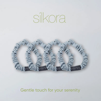 Vier kleine Silkora scrunchies in zilvergrijs op een lichte achtergrond met het Silkora-logo en de tekst "Gentle touch for your serenity".